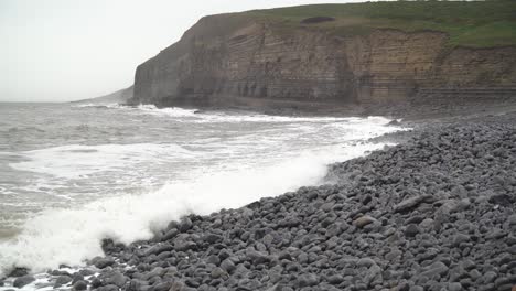 Wide-shot-of-Winter-Tide-splashing-in-over-rocky-beach-at-Dunraven-Bay,-South-Wales