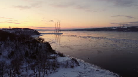 Aerial---Flying-over-the-coast-of-the-St-Lawrence-river,-looking-at-power-transmission-lines,-at-sunset