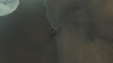 4k-Aerial-two-people-walking-on-black-sand-Drone-overhead-shot