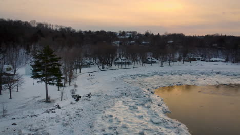 Aerial---Flying-around-a-tall-Eastern-white-pine-tree,-over-the-icy-shoreline-of-the-St-Lawrence-river,-at-sunset