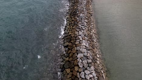 Breakwater-Structure-Made-Of-Rocks-Near-The-Coast-With-Waves-Splashing