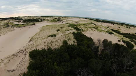 Close-up-fly-by-FPV-done-shot-of-the-dense-trees-transitioning-into-barren-desert-trails-with-soft-white-sand-dunes-and-high-peaks-in-Dune-Shacks-Trail-in-Provincetown,-Cape-Cod,-Massachusetts