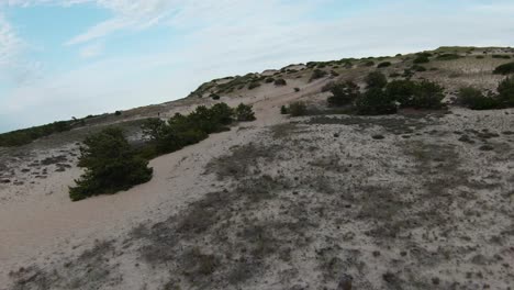 FPV-Drone-shot-of-the-amazing-desert-barren-trails,-sand-dunes,-rocks,-and-steep-slopes-with-small-bushy-foliage-located-in-Dune-Shacks-Trail-in-Provincetown,-Cape-Cod,-Massachusetts