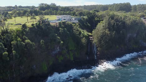 Drone-shot-of-a-large-luxurious-private-resort-on-the-side-of-a-cliff-surrounded-by-lush-green-foliage