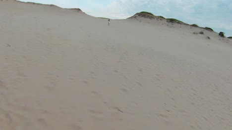 Aerial-flyby-shot-of-a-girl-running-on-the-hot-sand-dunes-and-trails-in-the-Dune-Shacks-Trail-in-Provincetown,-Cape-Cod,-Massachusetts