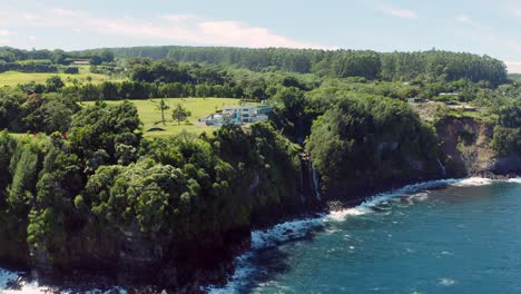 Surreal-Aerial-drone-shot-of-a-luxurious-private-resort-on-the-edge-of-a-cliff-surrounded-by-lush-green-foliage