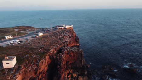 Drone-shot-of-a-cliff-in-Peniche,-Portugal-with-a-boat-in-the-sea-and-the-sunset-on-the-horizon---aerial