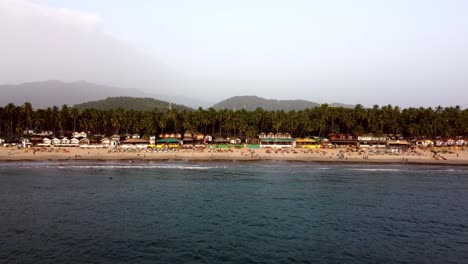 Drone-Volando-Hacia-La-Orilla-De-Una-Playa-En-Una-Playa-Tropical-Soleada-Con-Turistas,-India,-Goa,-Palolem