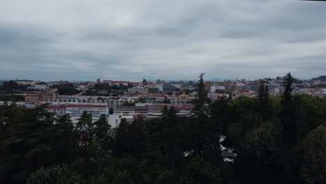 Revealing-shot-of-the-cloudy-city-of-Braga,-portugal-in-the-middle-of-a-forest---drone-shot