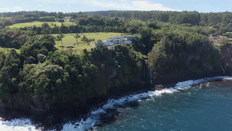 Drone-shot-of-a-luxurious-private-resort-on-the-side-of-a-cliff-surrounded-by-lush-green-foliage