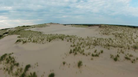 FPV-Drone-shot-of-the-scenic-barren-trails,-sand-dunes,-and-steep-slopes-with-small-bushy-foliage-located-in-Dune-Shacks-Trail-in-Provincetown,-Cape-Cod,-Massachusetts