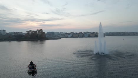 Footage-of-two-fishermen-sitting-in-their-boat-next-to-the-beautiful-fountain-standing-in-the-middle-of-the-water-in-the-naval-city-of-Karlskrona,-Sweden