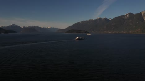 Two-ferries-sailing-at-sunset-between-mountains-on-the-Howe-Sound-in-British-Columbia,-Canada