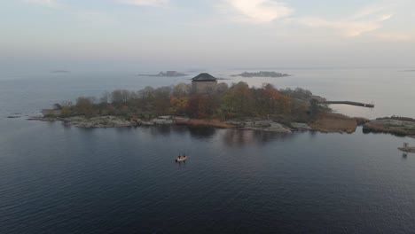 Aerial-view-over-two-fishermen-standing-on-their-boat-trying-to-catch-some-fish-in-the-beautiful-archipelago-in-the-naval-city-of-Karlskrona,-Sweden