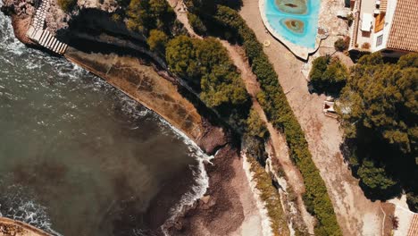 Overhead-view-of-waves-crashing-against-the-shore-of-a-house-with-stairs-to-the-sea-in-Ametlla-de-Mar,-Tarragona,-Spain