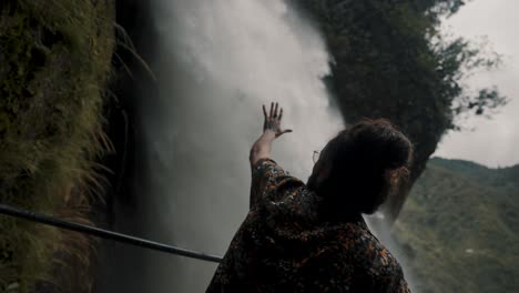 Male-With-Hand-Reaching-Toward-Pailon-del-Diablo-Waterfall-In-Baños-de-Agua-Santa,-Ecuador---closeup