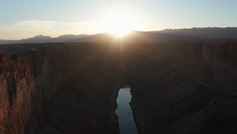 Cinematic-aerial-shot-over-Marble-Canyon,-Colorado-River,-as-the-sun-sits-at-the-peak-of-the-distant-mountains,-creating-dramatic-lens-flare