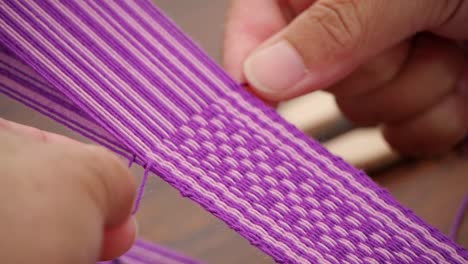 Fingers-stringing-and-pressing-purple-and-white-yarn