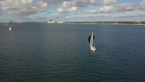 Orbiting-aerial-Black-spinnaker-propels-sailboat-downwind-near