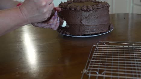 Woman's-hands-seen-decorating-a-triple-layered-chocolate-cake