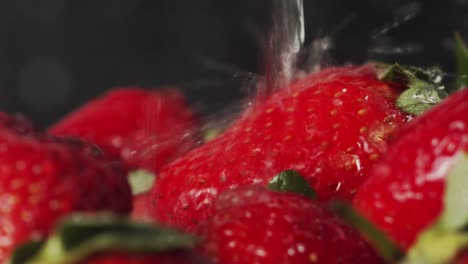 Kitchen-tap-water-splashing-onto-red-strawberries-Close