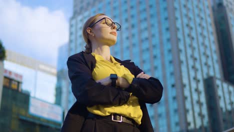 Thoughtful-businesswoman-in-eyeglasses-crossing-arms-standing-at
