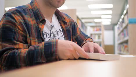 Man-wearing-flannel-flips-through-book-in-library
