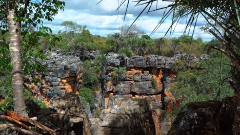 Tilting-down-shot-looking-out-to-a-hole-in-the-ground-created-from-the-Lapa-Doce-cave-with-a-jungle-inside-and-colorful-cliffs-in-the-Chapada-Diamantina-National-Park-in-Bahia,-northeastern-Brazil