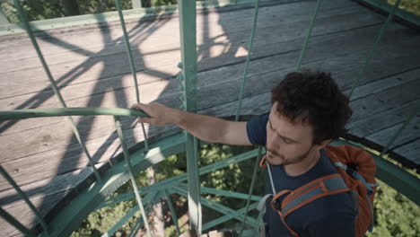 Man-walkig-upstairs-on-a-spiral-stairway-with-an-orange-backpack-to-reach-top-of-a-lookout-tower