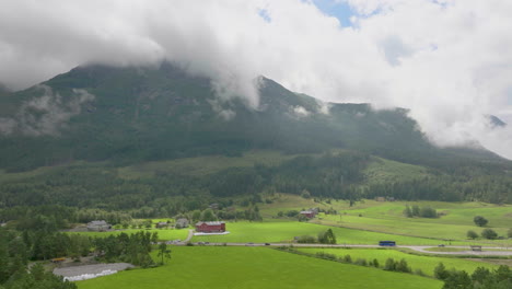Vista-Aérea-De-La-Carretera-Rural-Que-Cruza-Los-Verdes-Campos-Agrícolas-Que-Revelan-El-Fondo-Del-Paisaje-Del-Fiordo,-Noruega