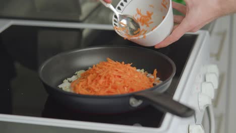 Man-scooping-grated-carrots-into-a-frying-pan