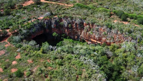 Aerial-drone-tilting-down-and-dolly-in-medium-shot-of-the-Lapa-Doce-cave-entrance-with-a-self-contained-rainforest-below-in-the-Chapada-Diamantina-National-Park-in-Bahia,-northeastern-Brazil