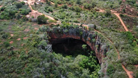 Aerial-drone-tilting-up-and-dolly-out-shot-of-the-Lapa-Doce-cave-entrance-with-a-self-contained-rainforest-below-in-the-Chapada-Diamantina-National-Park-in-Bahia,-northeastern-Brazil