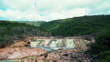 Nach-Oben-Kippender-Schuss,-Der-Den-Wunderschönen-Donana-wasserfall-Mit-Bunten-Felsen,-Schmutzigem-Wasser-Und-Umgeben-Von-Grünen-Tropischen-Hügeln-Im-Chapada-diamantina-nationalpark-In-Bahia-Im-Nordosten-Brasiliens-Enthüllt