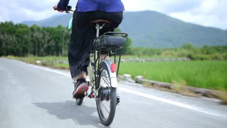 Asian-woman-riding-bike-during-sightseeing-trip-through-countryside,-filmed-as-medium-shot-following-bicycle-from-backside-of-rider