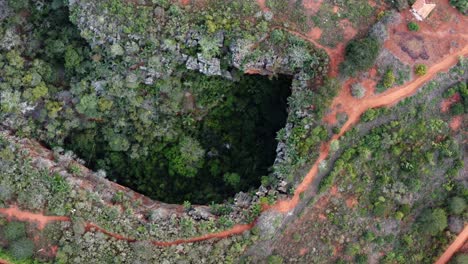 Aerial-drone-top-down-bird's-eye-shot-of-the-Lapa-Doce-cave-entrance-of-colorful-rocks-with-a-self-contained-rainforest-below-in-the-Chapada-Diamantina-National-Park-in-Bahia,-northeastern-Brazil