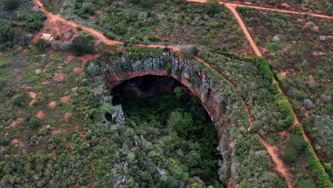 Aerial-drone-tilting-down-shot-of-the-large-Lapa-Doce-cave-entrance-of-colorful-rocks-with-a-self-contained-rainforest-below-in-the-Chapada-Diamantina-National-Park-in-Bahia,-northeastern-Brazil