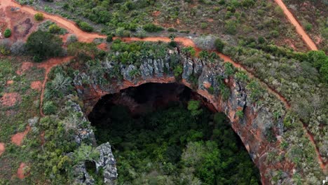 Aerial-drone-lowering-shot-of-the-large-Lapa-Doce-cave-entrance-of-colorful-rocks-with-a-self-contained-rainforest-below-in-the-Chapada-Diamantina-National-Park-in-Bahia,-northeastern-Brazil