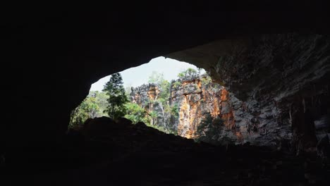 Tilting-up-shot-from-inside-the-Lapa-Doce-cave-looking-out-revealing-a-huge-cave-entrance-with-colorful-cliffs-and-jungle-foliage-in-the-Chapada-Diamantina-National-Park-in-Bahia,-northeastern-Brazil