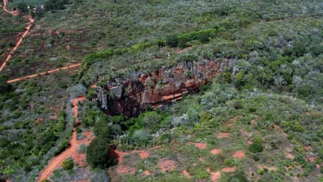 Aerial-drone-rotating-wide-shot-of-the-large-Lapa-Doce-cave-entrance-of-colorful-rocks-with-a-self-contained-rainforest-below-in-the-Chapada-Diamantina-National-Park-in-Bahia,-northeastern-Brazil
