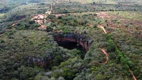 Aerial-drone-dolly-in-wide-shot-of-the-large-Lapa-Doce-cave-entrance-of-colorful-rocks-with-a-self-contained-rainforest-below-in-the-Chapada-Diamantina-National-Park-in-Bahia,-northeastern-Brazil