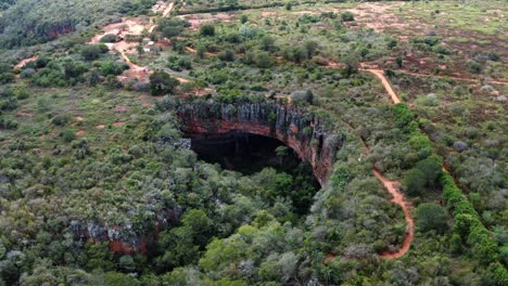 Aerial-drone-tilting-down-and-dolly-in-wide-shot-of-the-Lapa-Doce-cave-entrance-with-a-self-contained-rainforest-below-in-the-Chapada-Diamantina-National-Park-in-Bahia,-northeastern-Brazil