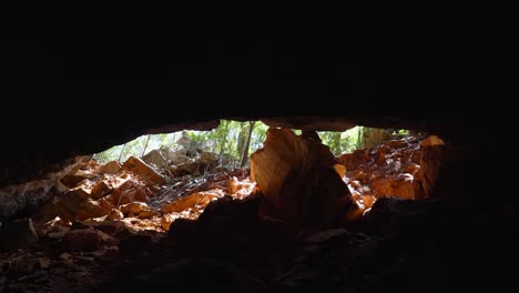 Tilting-up-shot-revealing-a-beautiful-golden-cave-entrance-inside-a-jungle-in-the-Lapa-Doce-cave-in-the-Chapada-Diamantina-National-Park-in-Bahia,-northeastern-Brazil
