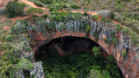 Aerial-drone-medium-dolly-in-shot-of-the-large-Lapa-Doce-cave-entrance-of-colorful-rocks-with-a-self-contained-rainforest-below-in-the-Chapada-Diamantina-National-Park-in-Bahia,-northeastern-Brazil