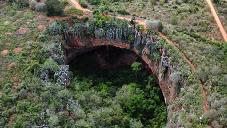 Aerial-drone-medium-shot-of-the-large-Lapa-Doce-cave-entrance-of-colorful-rocks-with-a-self-contained-rainforest-below-in-the-Chapada-Diamantina-National-Park-in-Bahia,-northeastern-Brazil