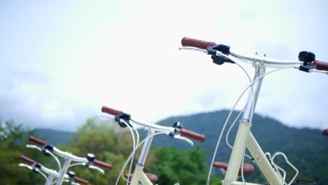 4-cream-colored-biked-parked-next-to-each-other-with-mountains-and-trees-in-background,-filmed-with-upward-tilt-camera-motion-on-sunny-day