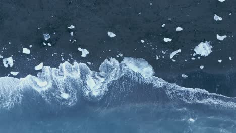 Wellen,-Die-Auf-Eisbergfragmente-Krachen,-Die-Auf-Dem-Schwarzen-Sand-Des-Diamantstrandes-In-Island-Verstreut-Sind