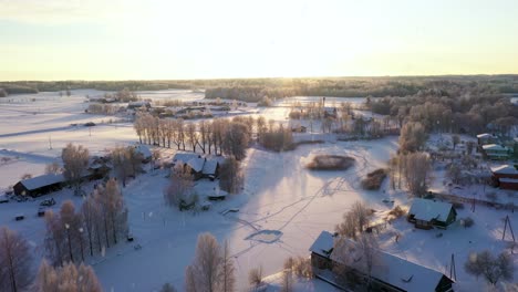 Bright-sunset-over-rural-village-during-light-snowfall,-aerial-view