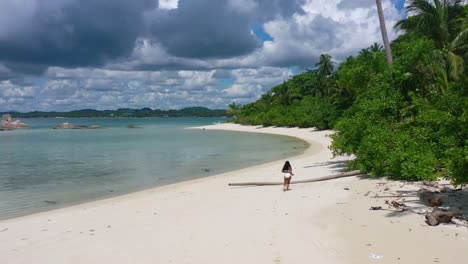 aerial-of-young-asian-girl-running-on-empty-white-sand-beach-on-tropical-island-in-belitung-indonesia