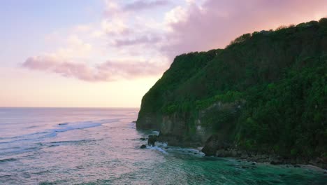 aerial-of-beautiful-calm-ocean-waves-crashing-onto-uluwatu-cliffs-with-pink-and-purple-sky